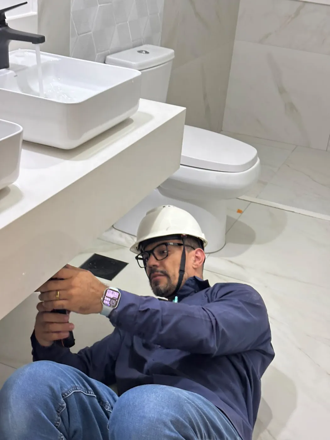 Engenheiro inspecionando com lanterna a parte de baixo da bancada do banheiro