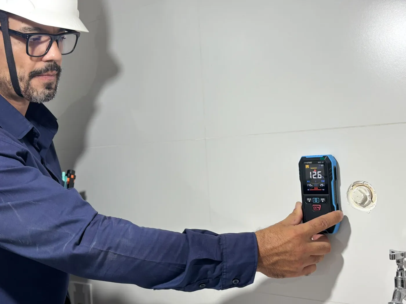 Engenheiro medindo a umidade da parede ao lado da torneira da área de serviço